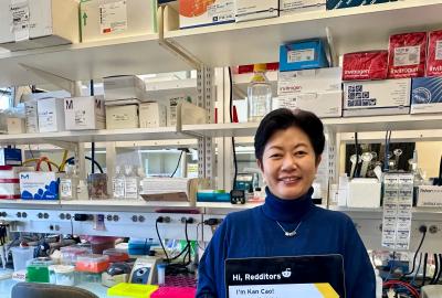 Kan Cao in her lab holding a laptop promoting her Reddit AMA