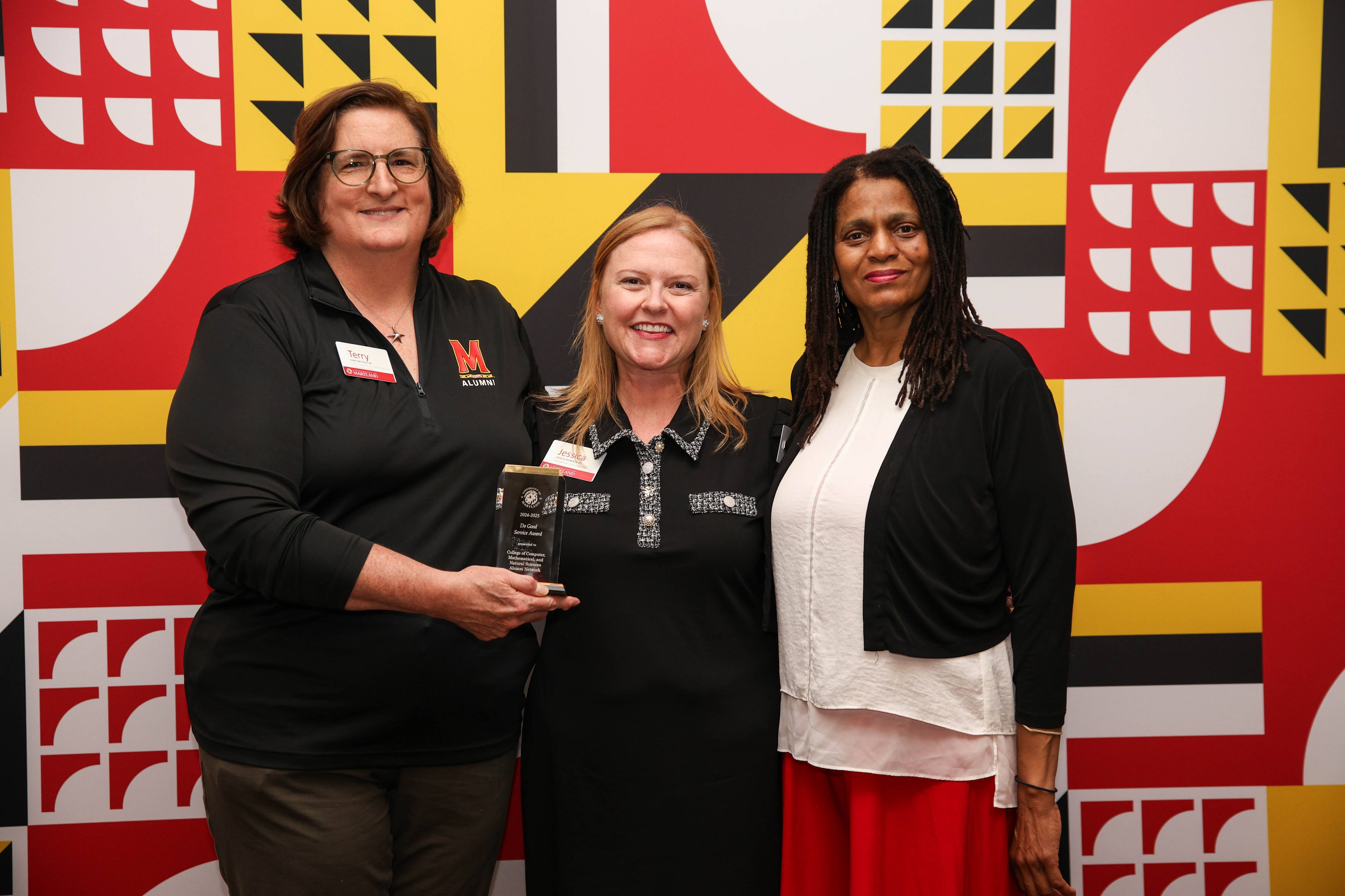 Three people standing in front of a backdrop holding an award