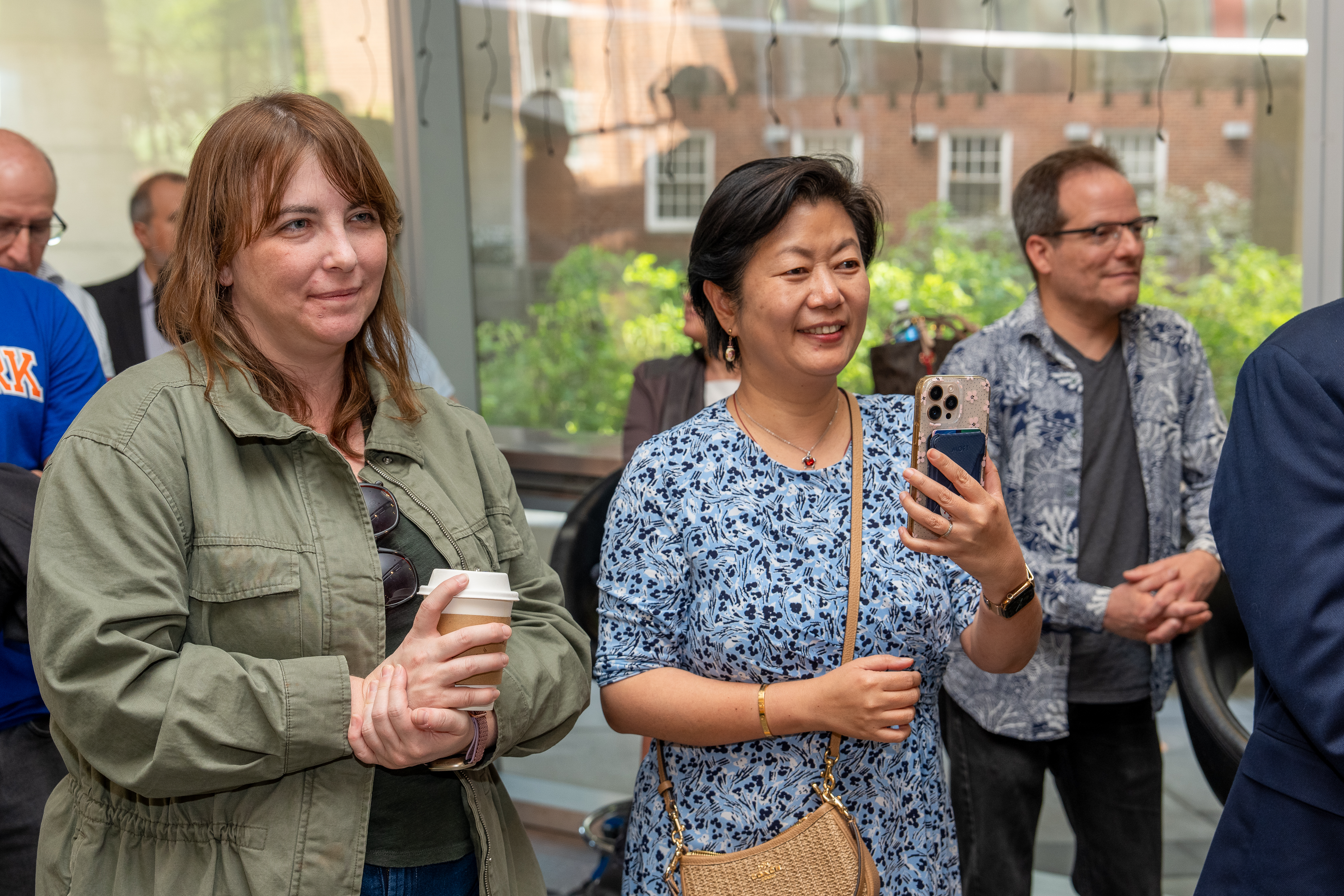 A group of people standing in an audience, with one woman taking photos on her phone