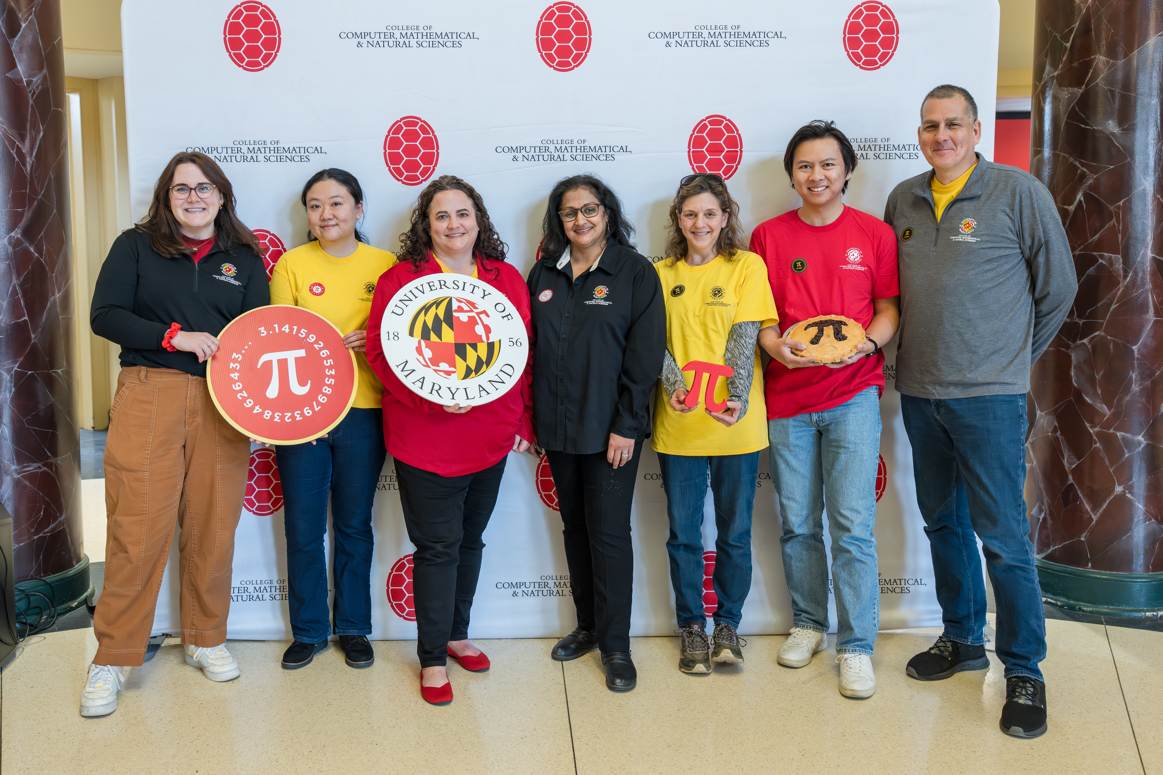 A group of people holding UMD and pie/Pi-related props in front of a step-and-repeat banner