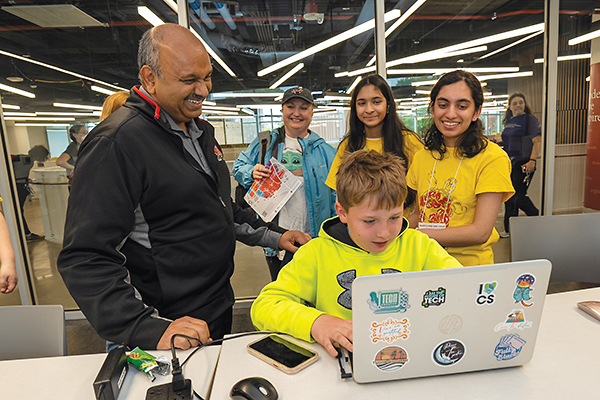 Dean Amitabh Varshney, professors and students standing behind an elementary school-aged boy using a laptop in the Iribe Center.