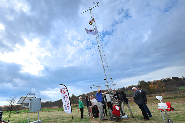 Members of the Maryland Mesonet group erecting a new weather-monitoring tower in an open, grassy field.
