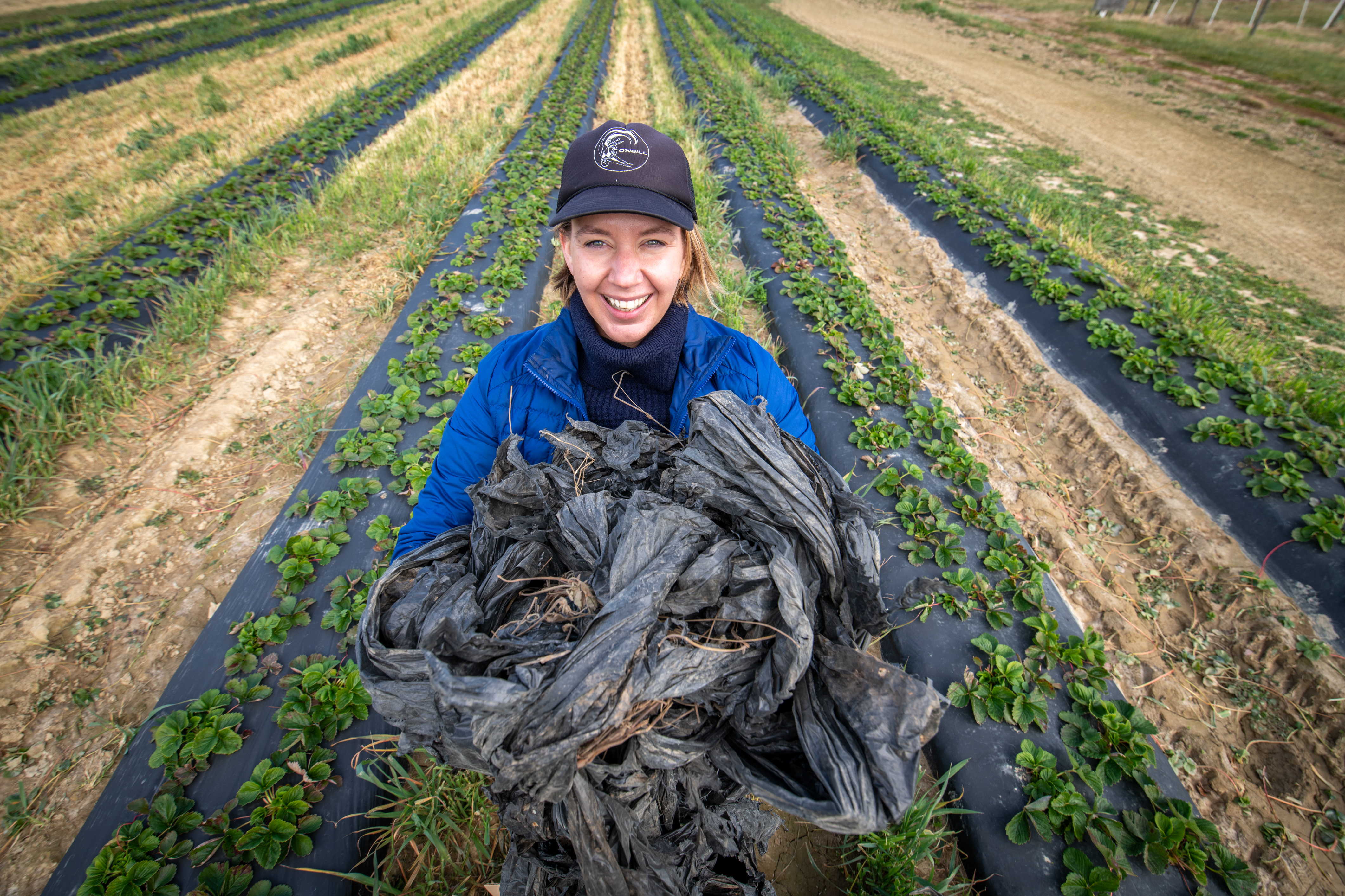 Krisztina Christmon holds a heap of plastic trash while standing in a field