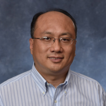 Portrait of Heng Huang in striped shirt and glasses.