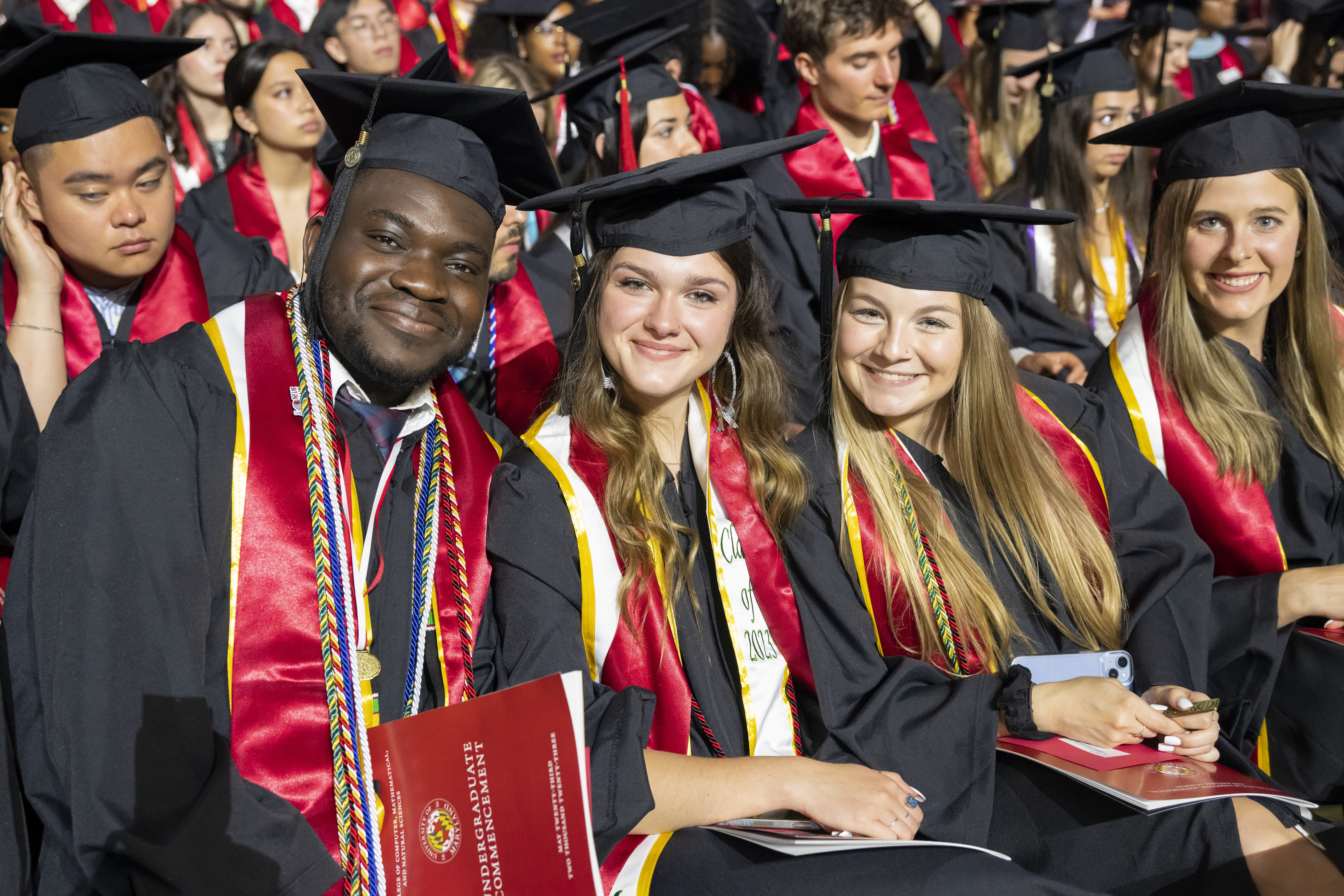 Three students seated for commencement in the Xfinity Center