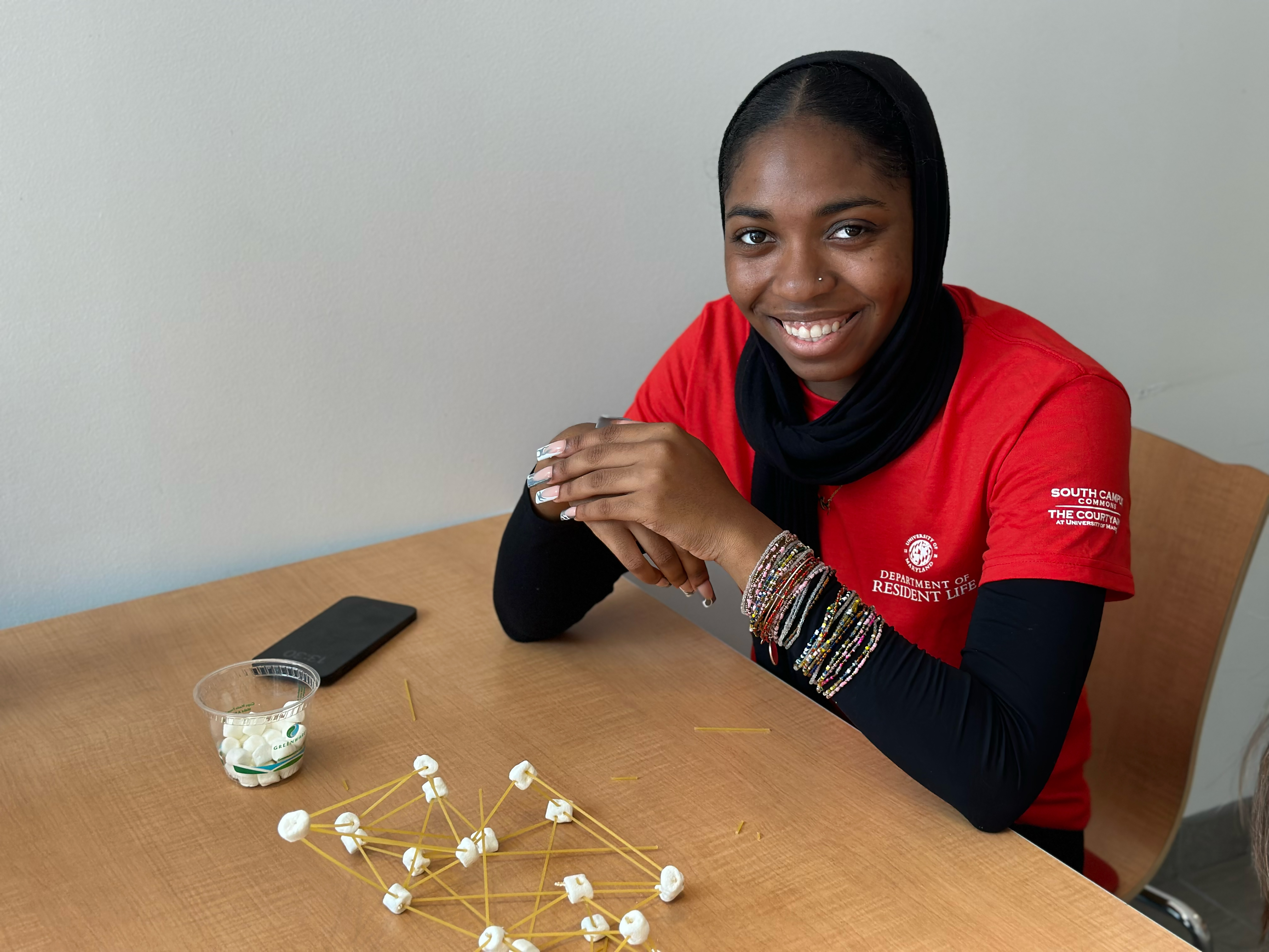 Student poses with structure made of miniature marshmallows and spaghetti noodles.