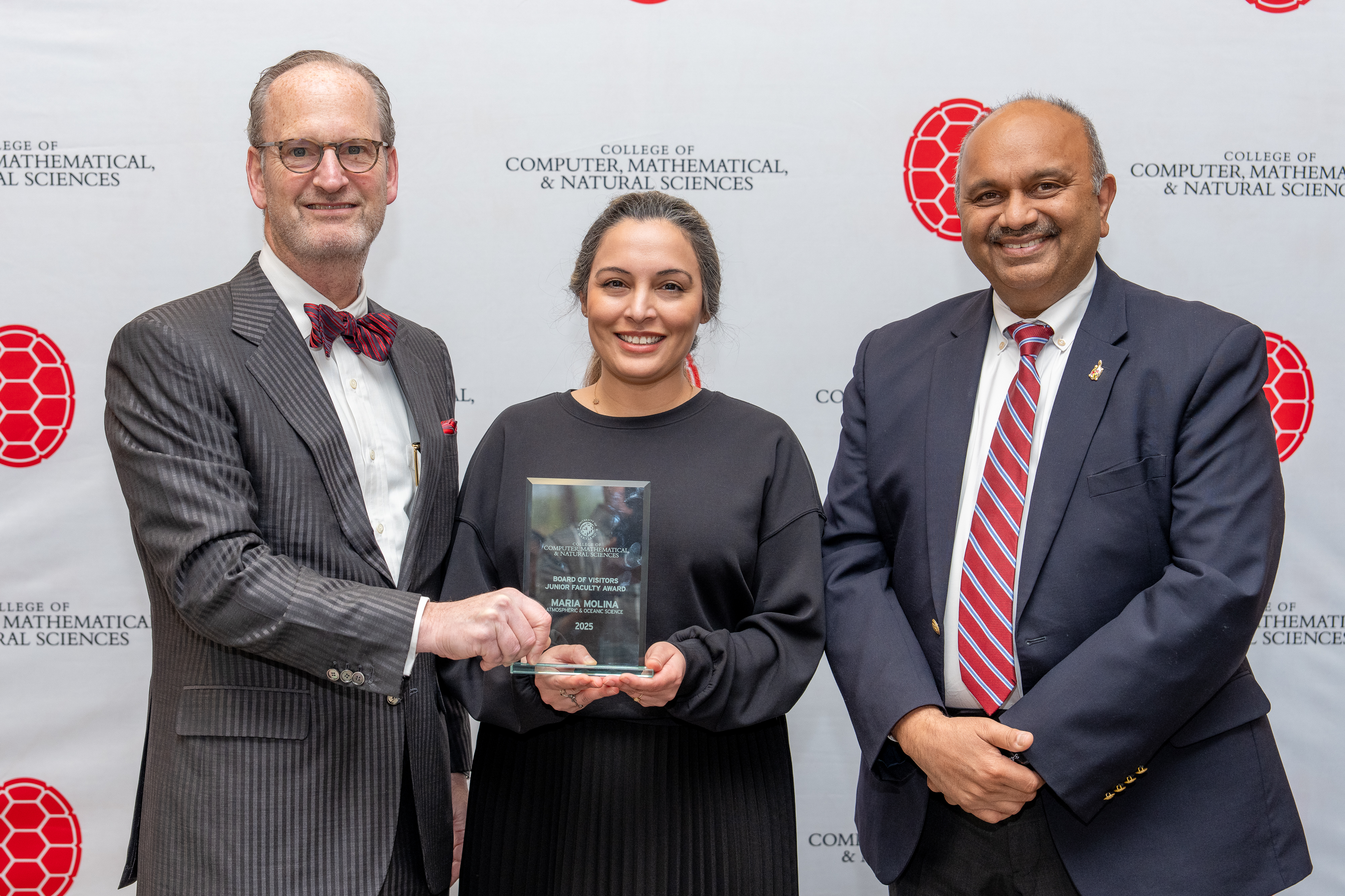 Three people holding an award in front of a step-and-repeat banner