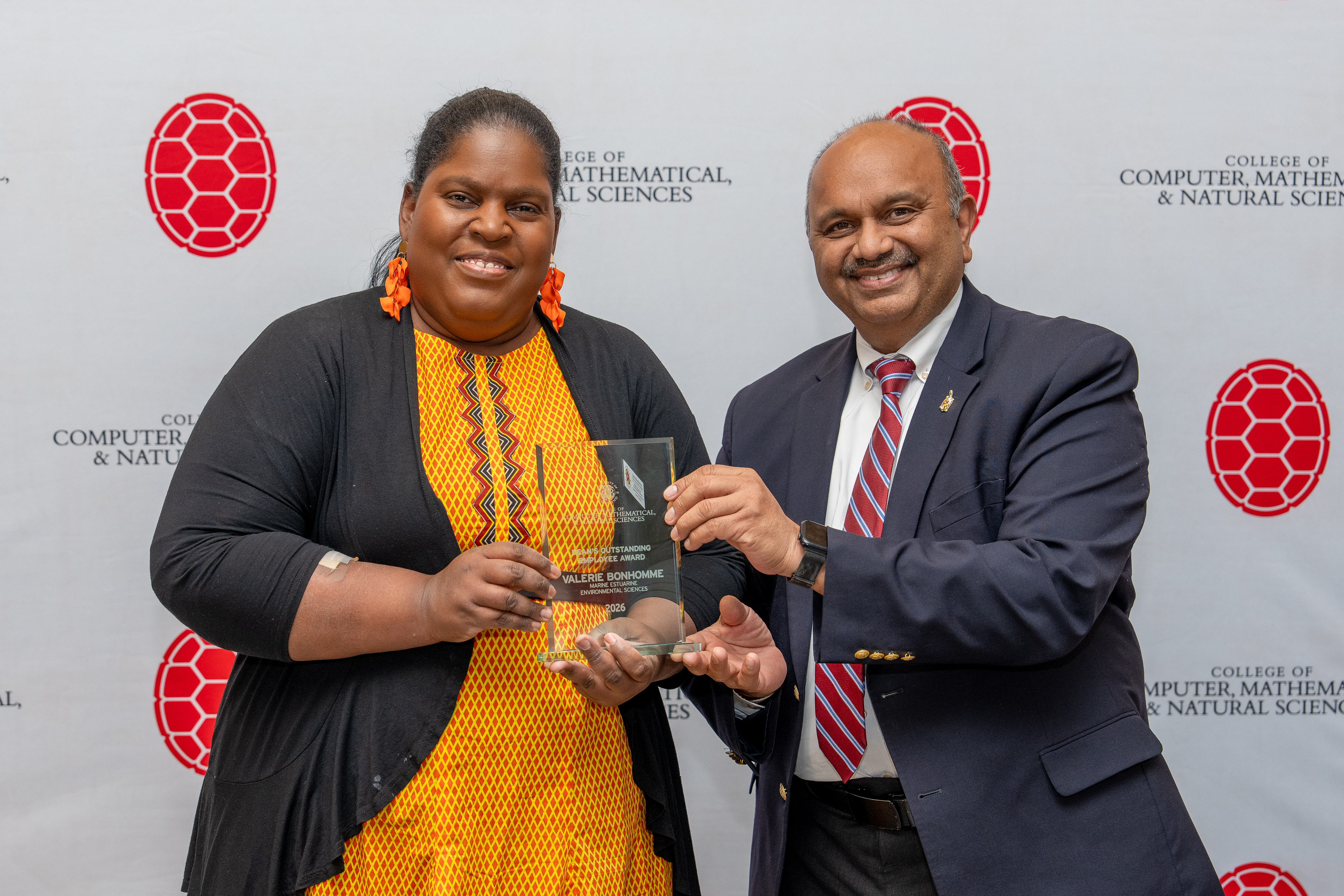 Two people holding an award in front of a step-and-repeat banner