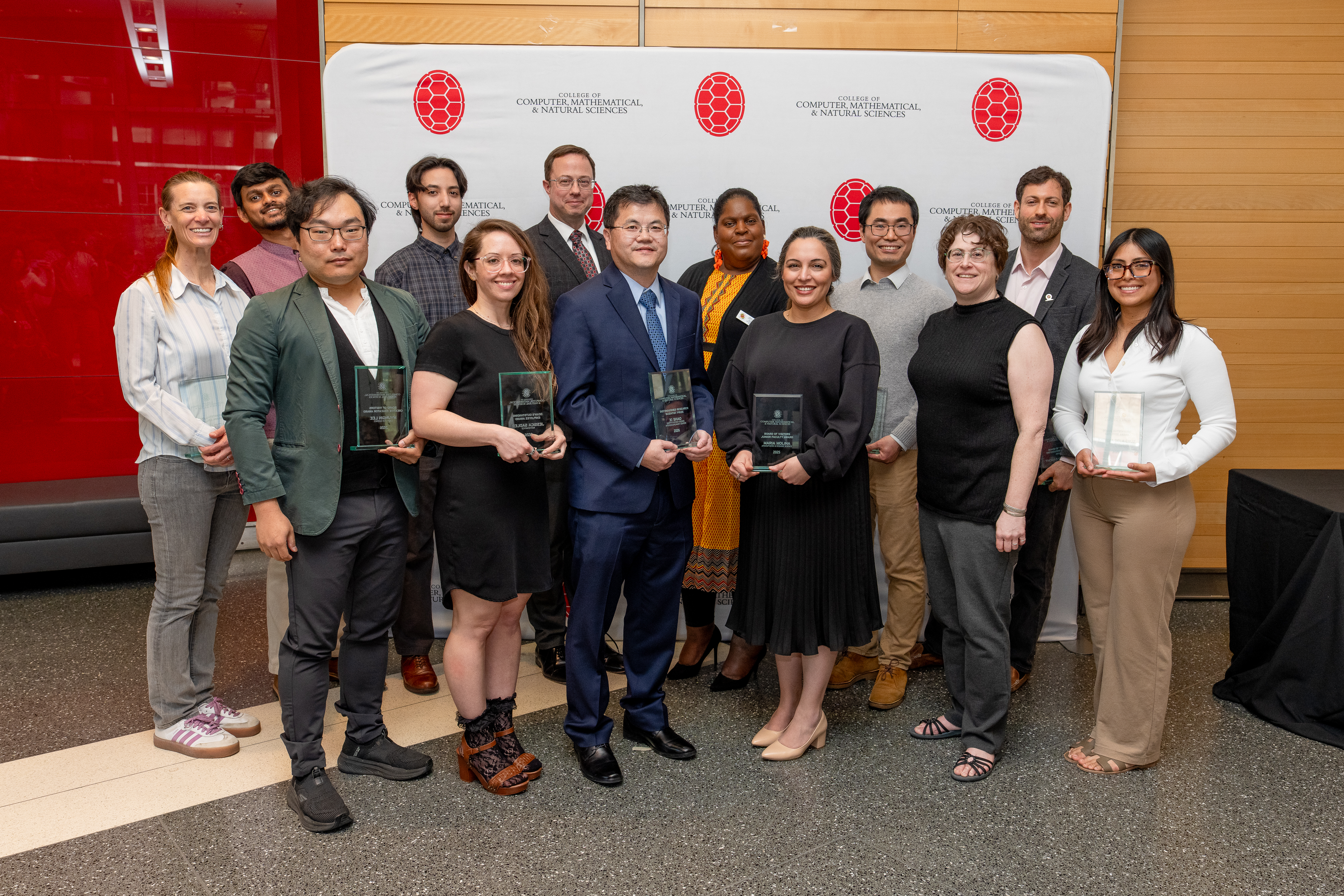 Group of people holding awards in front of a step-and-repeat banner