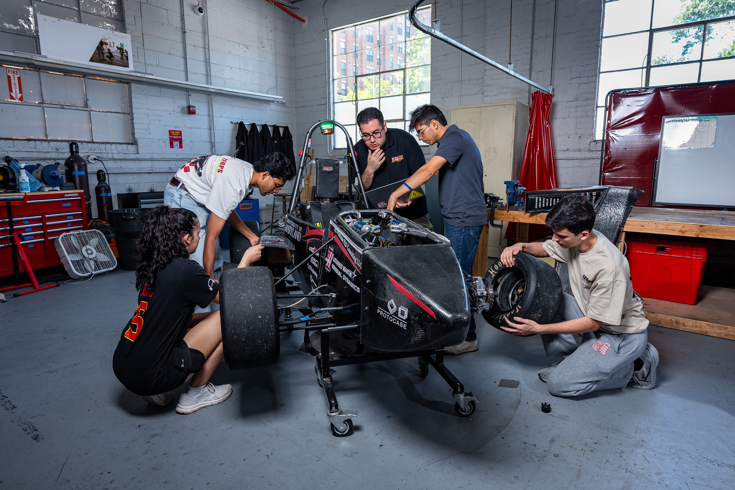 Five students huddle around their race car in the garage.