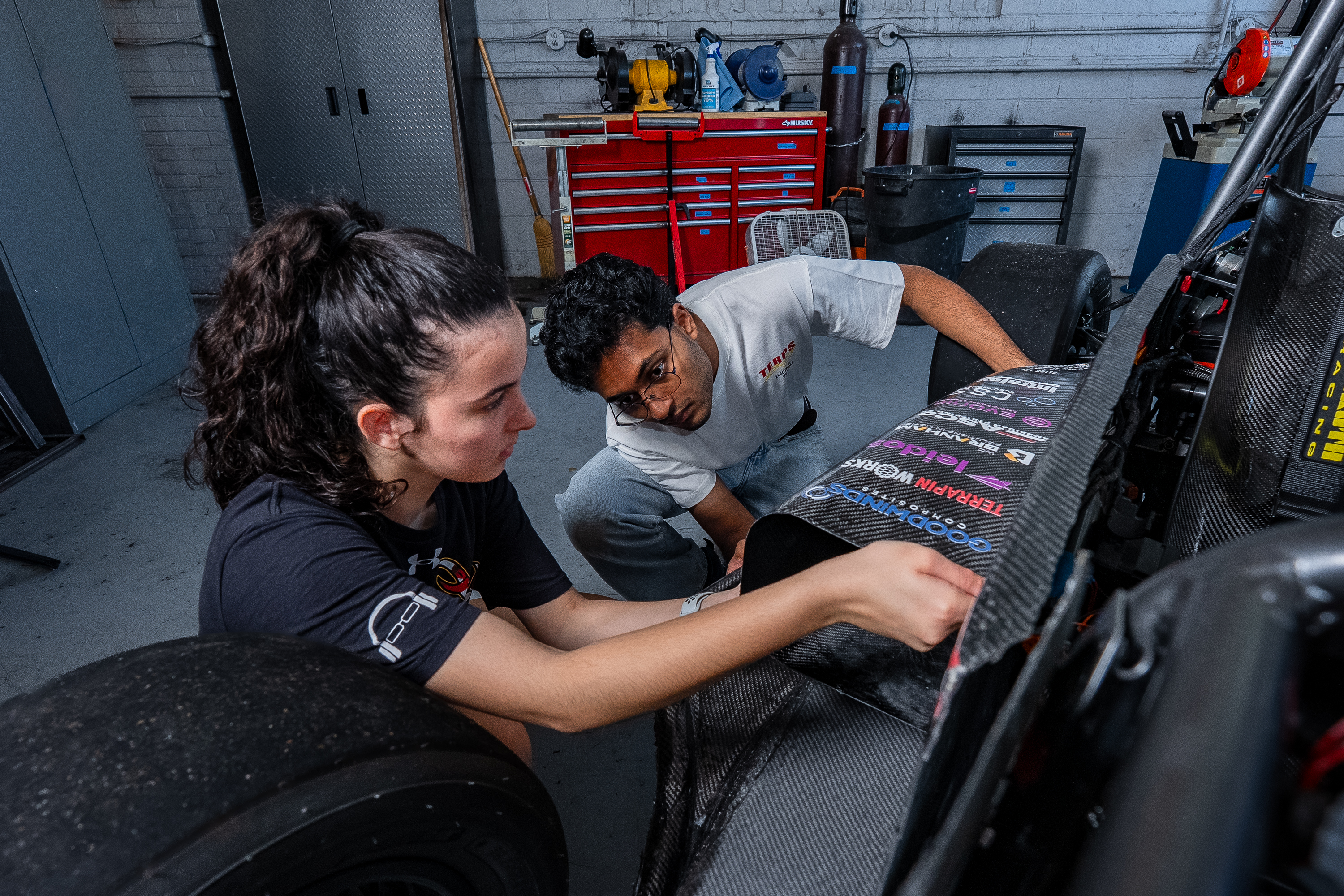 Two students inspect the body of the race car, with sponsor titles printed on it.