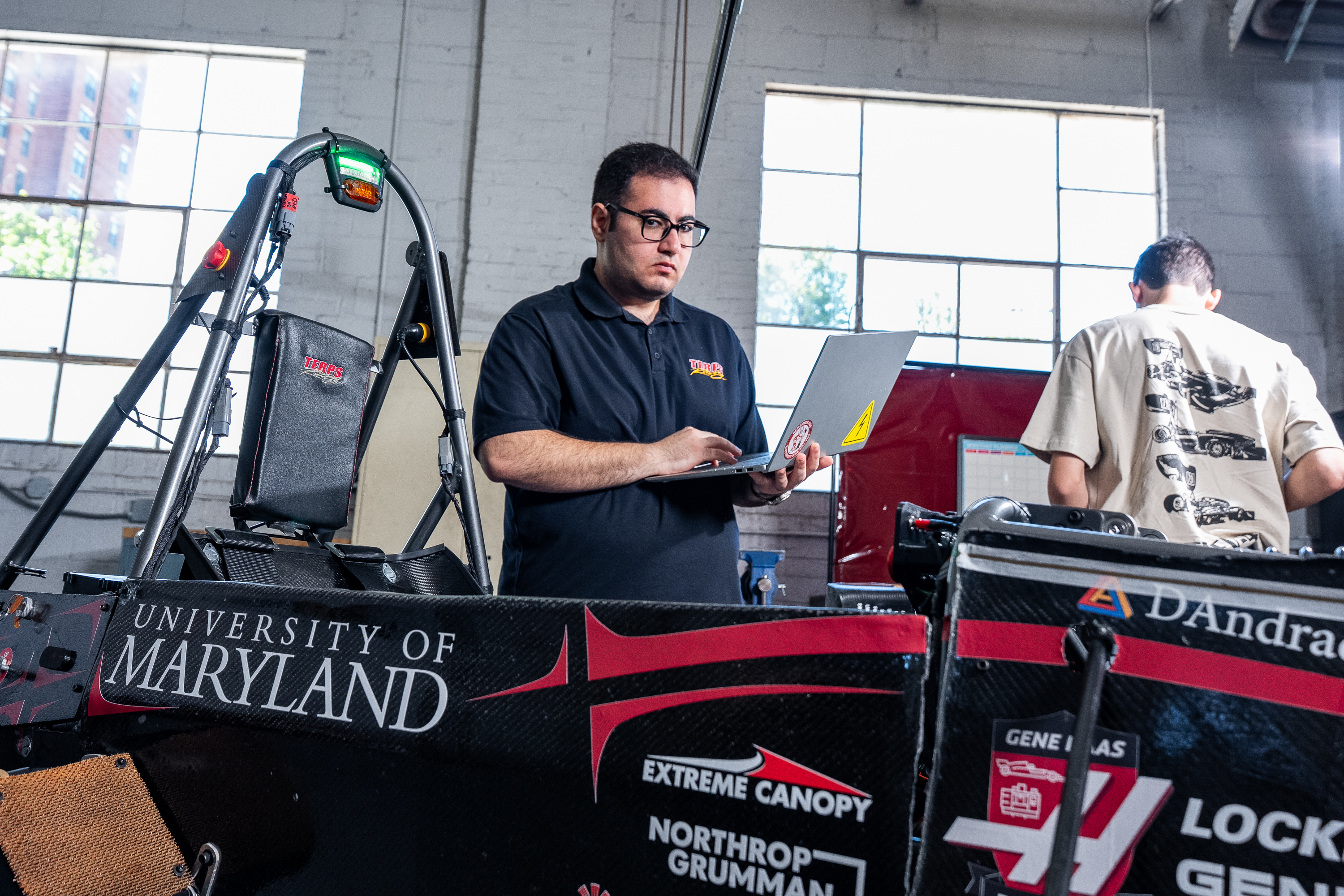 A student in a Terps Racing EV polo looks at a laptop while standing next to the race car. 