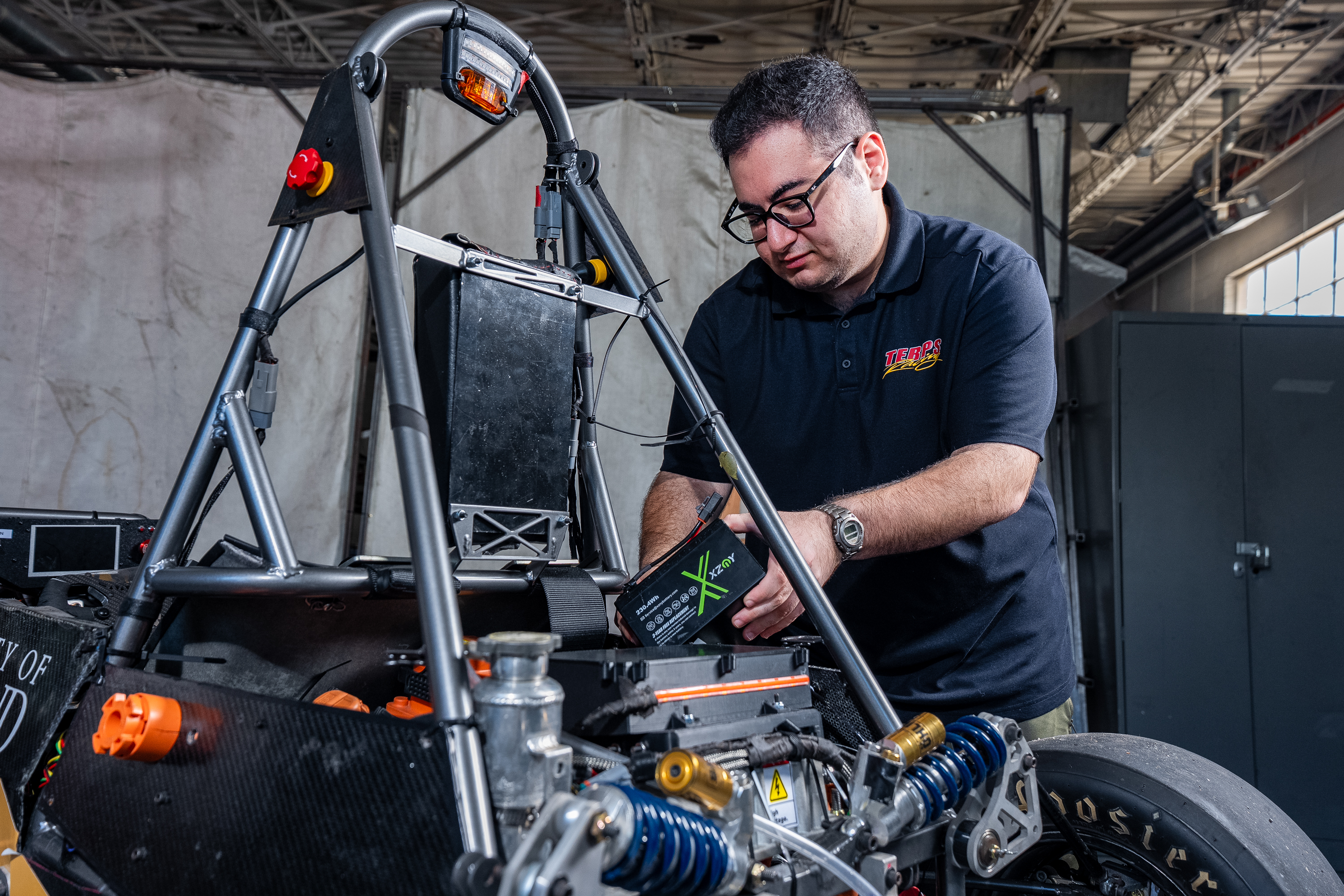 A student in a Terps Racing EV polo adjusts components on the car. 
