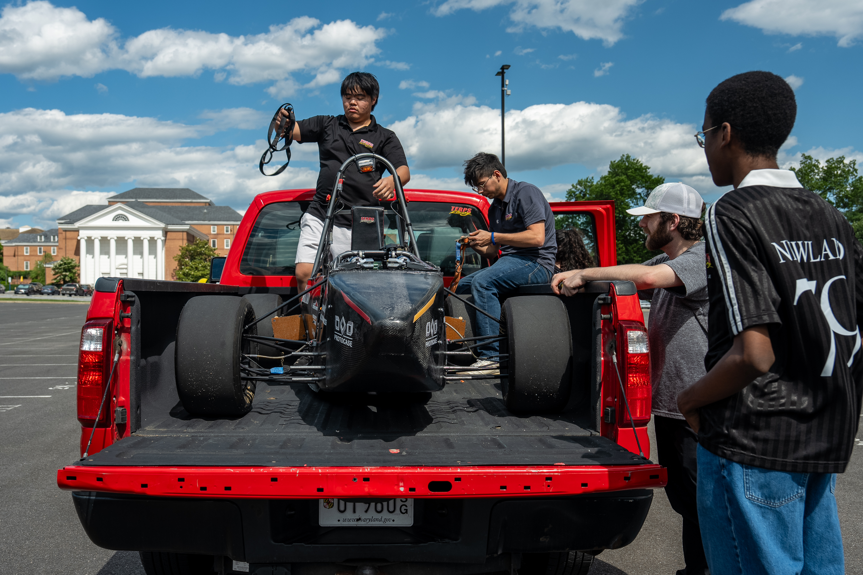 Students secure the race car in the back of a red pickup truck.