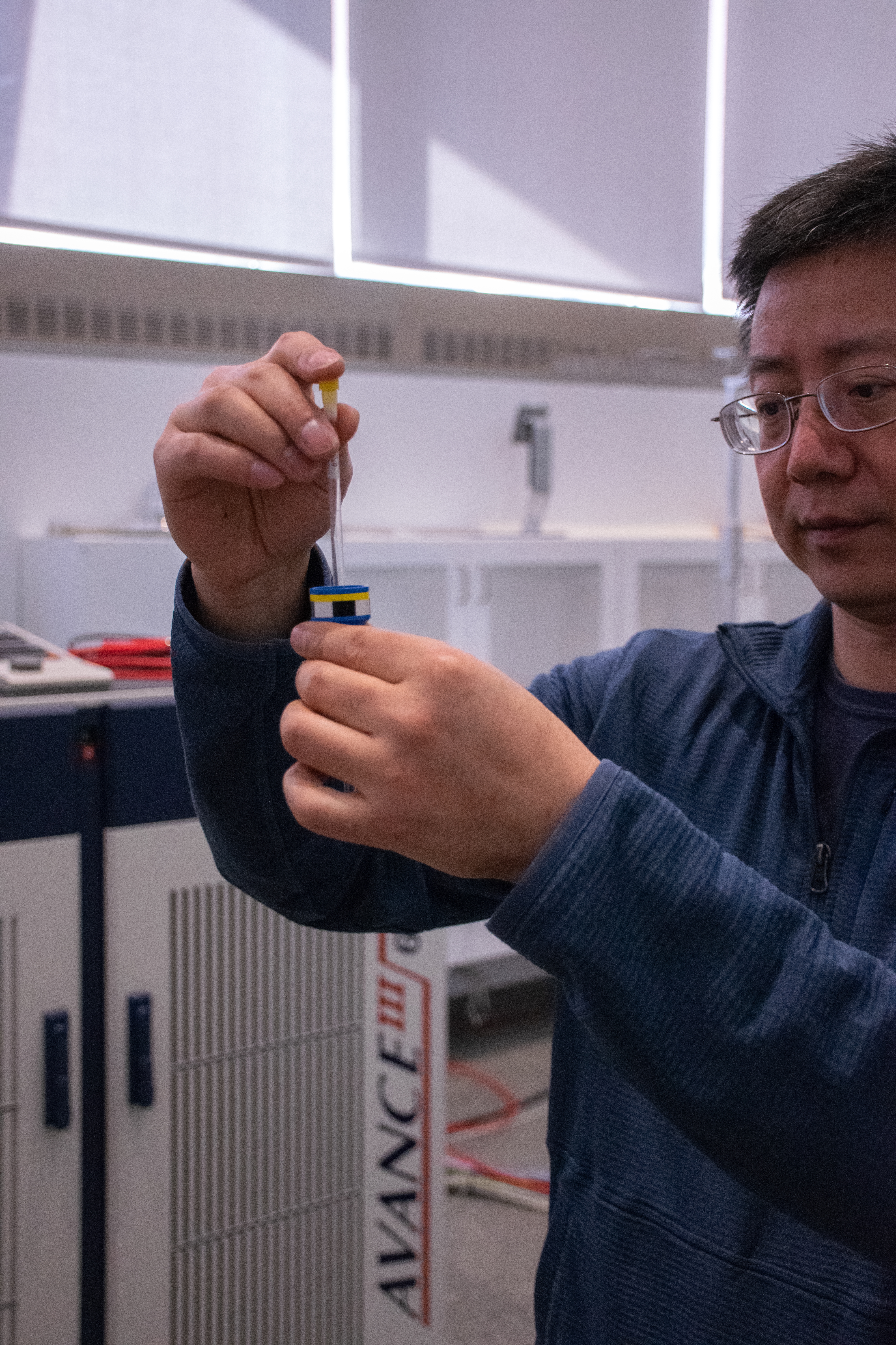 A man in a blue sweater holds small glass tube and inserts it into a blue device. 