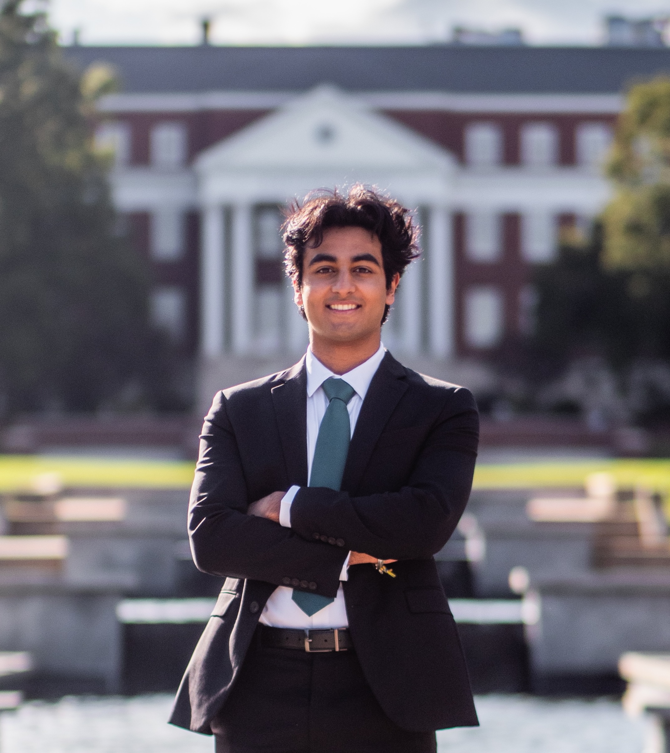 Dhruv Dewan stands in a suit in front of a red academic building.
