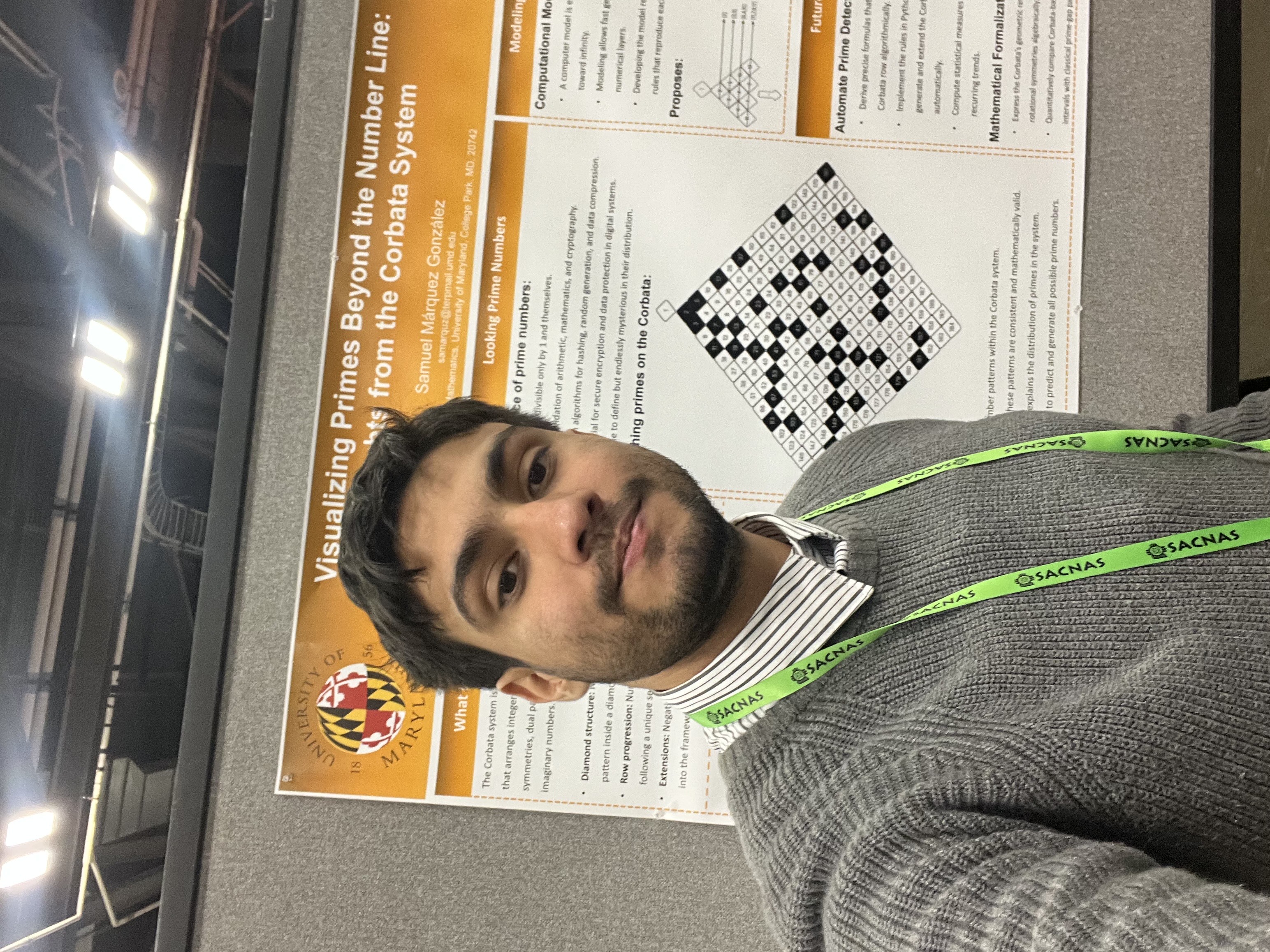 Samuel Márquez González wears a striped button down shirt and gray sweater, standing in front of his research poster which is white with orange headers.