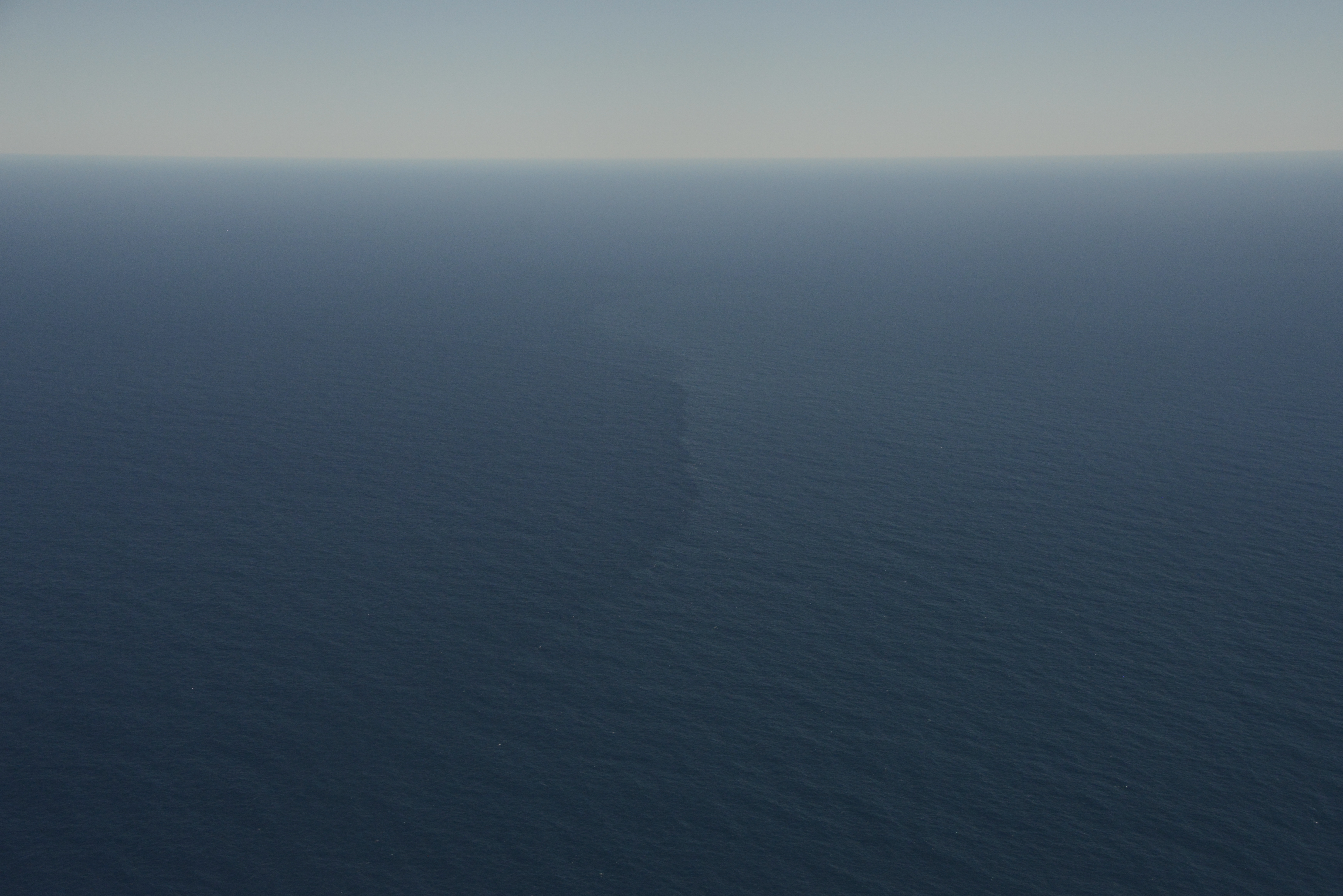 Aerial view of open ocean with a faint vertical streak marking a surface front amid calm blue water.