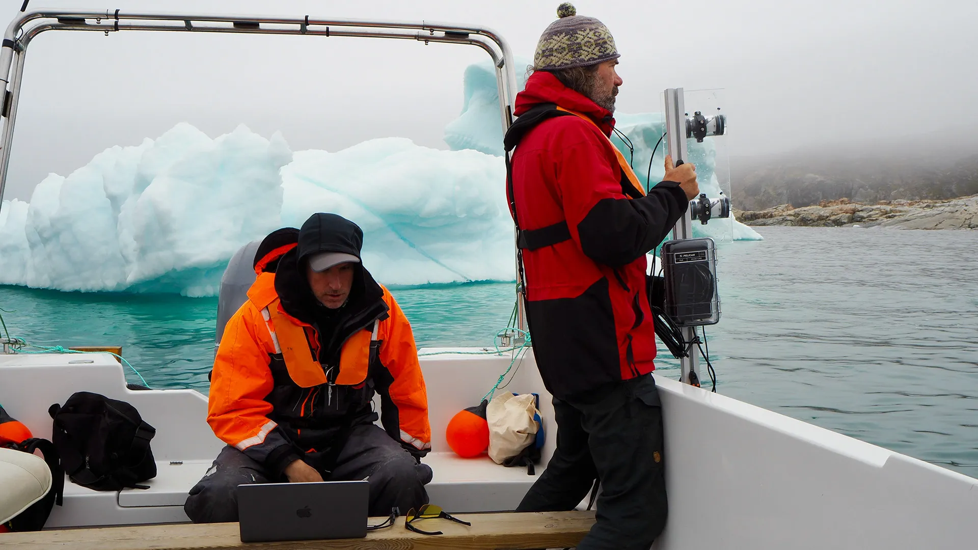 Cy Keener (seated on a boat at an iceberg in Greenland while Lars Smedsrud holds device equipped with sonar technology