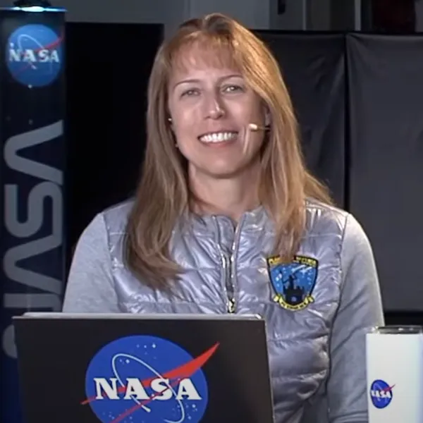 Kelly Fast in front of a laptop with a NASA logo sticker wearing a headset