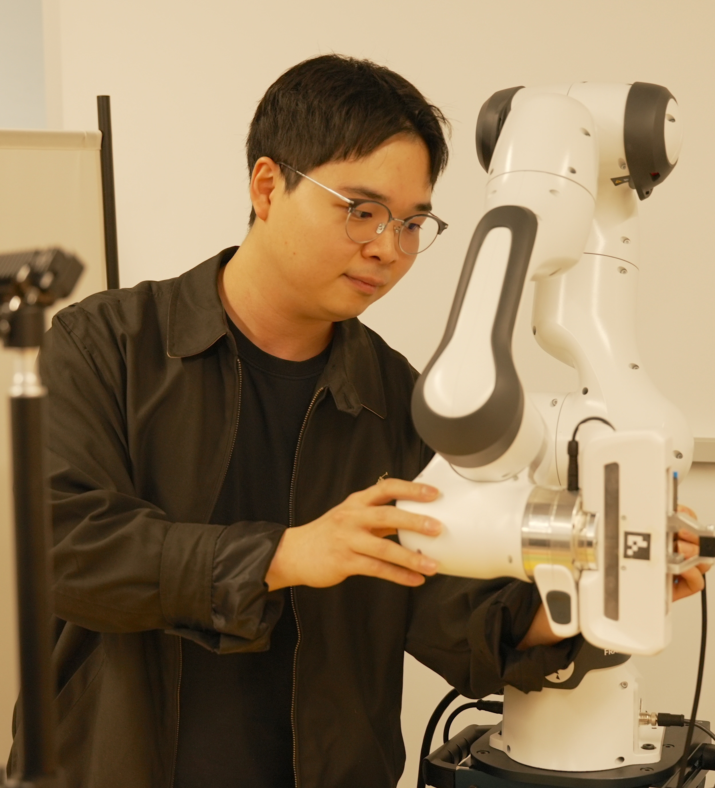 Seungjae “Jay” Lee works on a laptop beside a robotic arm. 