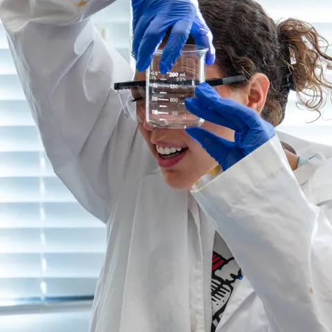 Student wearing labcoat looking at beaker