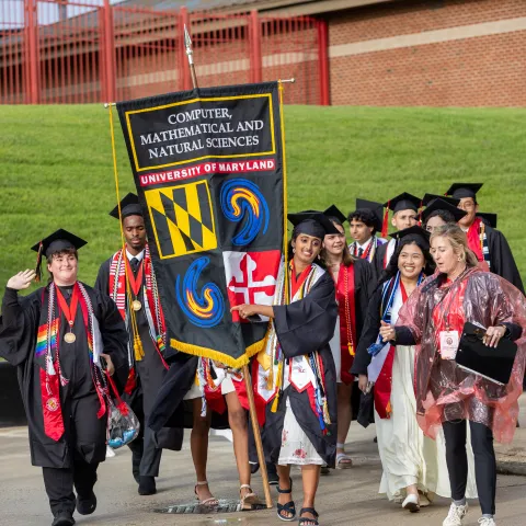 Student carrying a commencement banner to UMD main commencement ceremony