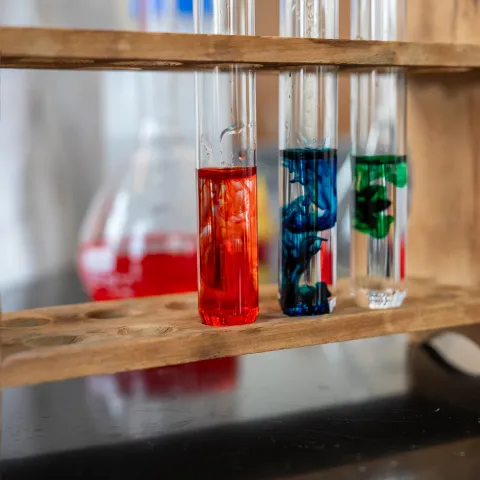 Three vials on a wooden stand with different color liquids