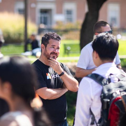 A man wearing a Microsoft shirt holding his chin in his hands while talking to a student