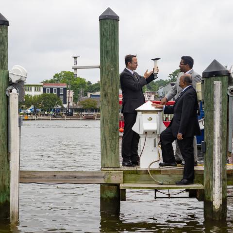 Three men standing on a dock looking at a device