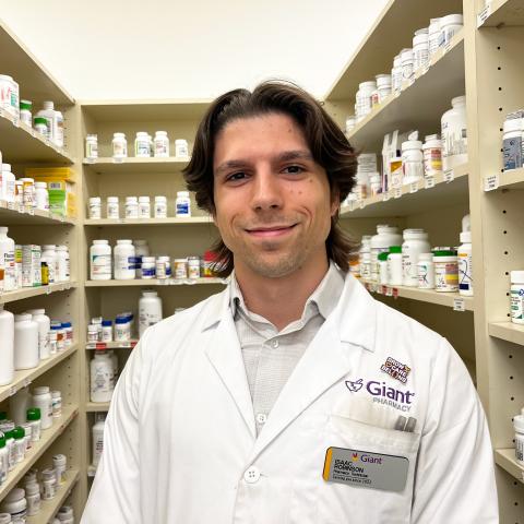 Man wearing a white Giant Pharmacy lab coat standing in front of shelves of medication