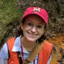Marcie Occhi smiling in a red hat and orange vest.