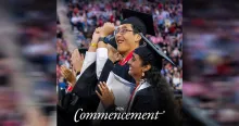 Two students in graduation regalia celebrating, with a blurred crowd in the background.