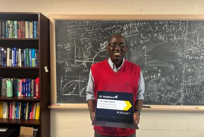 Mathematics Professor Abba Gumel standing in front of a chalkboard holding a laptop