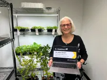 Anne Simon in front of plants holding a laptop