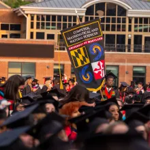Senior marshal holding the College of Computer, Mathematical, and Natural Sciences gonfalon at the May 2023 commencement ceremony. 