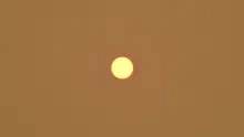 The sun appearing as a small yellow circle in the center of the image against a burnt orange sky.