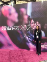 Nithika Ramanathan standing in front of the Grace Hopper Celebration 2025 banner