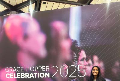 Nithika Ramanathan standing in front of the Grace Hopper Celebration 2025 banner