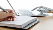 hand writing in journal across from robot hand typing on computer