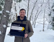 Justin Pflug wearing a coat and holding a laptop in front of a snowy forest