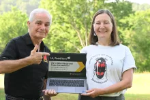Michael Raupp and Paula Shrewsbury holding a laptop in the middle of a field with trees in the background