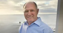 Man wearing blue button-down shirt with the ocean in the background