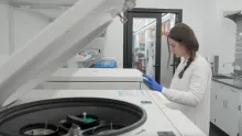 A person wearing blue gloves and a labcoat working in a lab