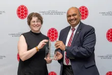 Two people holding an award in front of a CMNS step-and-repeat banner