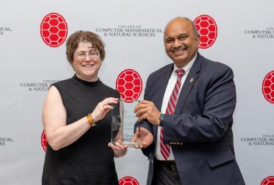 Two people holding an award in front of a CMNS step-and-repeat banner