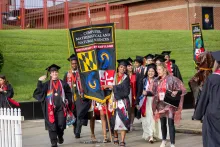 A group of graduates wearing regalia carrying gonfalon into commencement