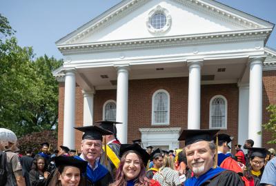 Two female Ph.D students in red regalia posing with two professors in black regalia. Credit: Lisa Helfert.