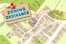 Architectural land development and zoning map showing numbered plot areas, buildings, and green spaces. A piece of light brown paper is attached to the top left corner with a red pushpin, displaying the text "ZONING ORDINANCE" in large blue letters above the subtext "Zoning and Land Use Planning."
