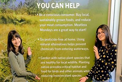 Two girls standing on either side of a wall filled with text about native plants